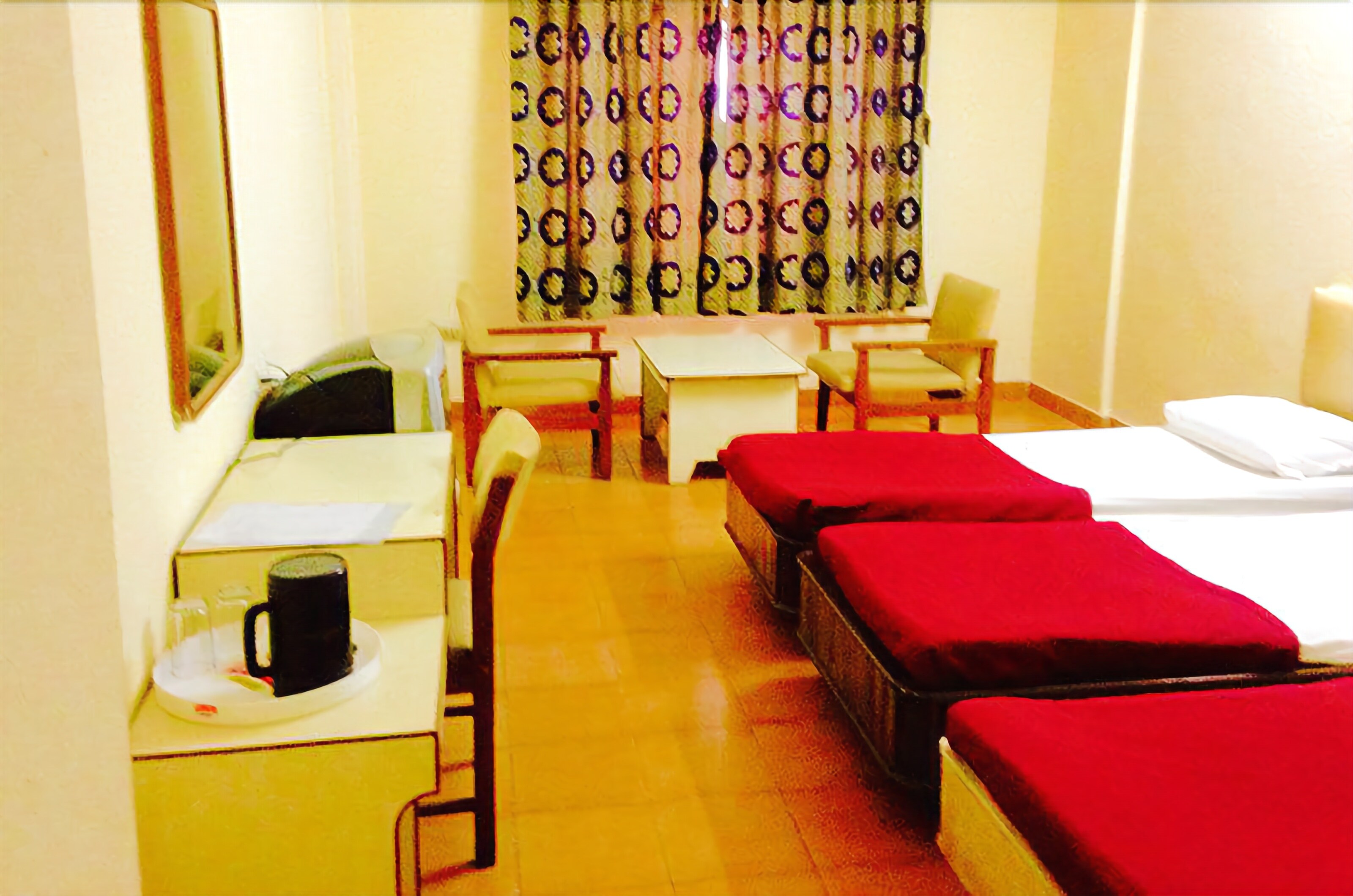 A hotel room with a desk, two single beds, a chair, a small table, and a mirror.