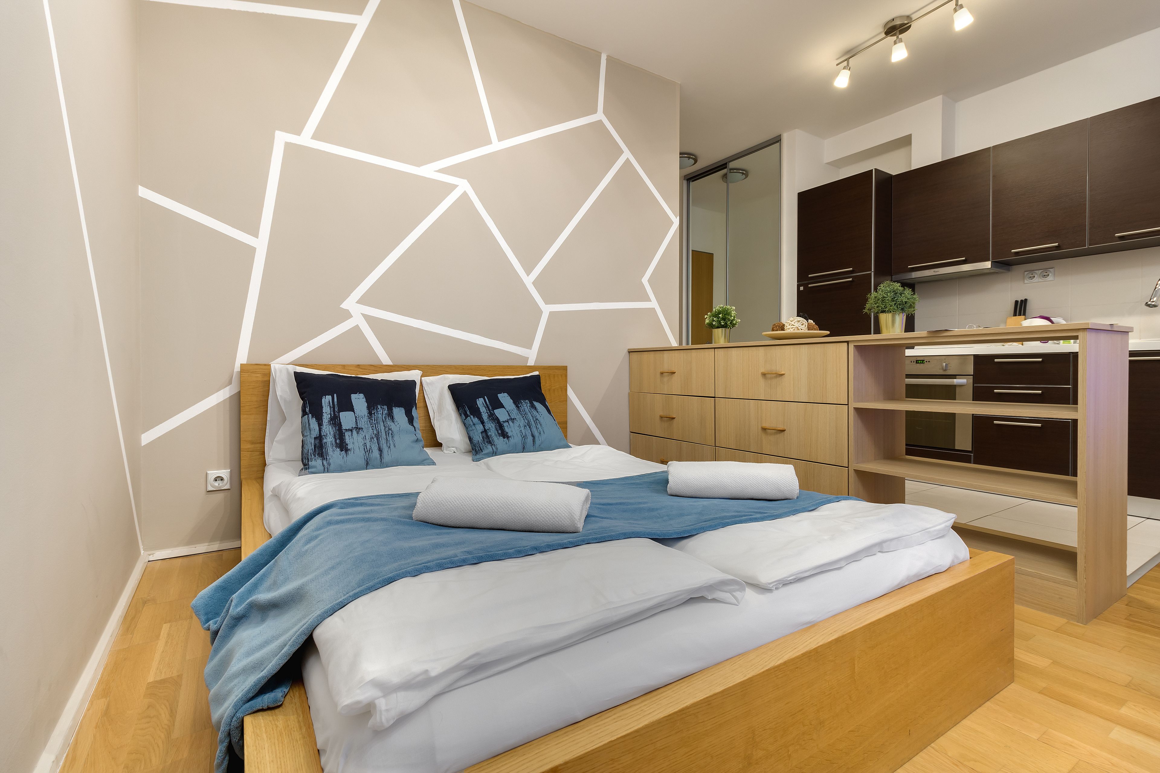 Un dormitorio moderno con una cama de madera, un diseño geométrico en la pared y un armario empotrado.