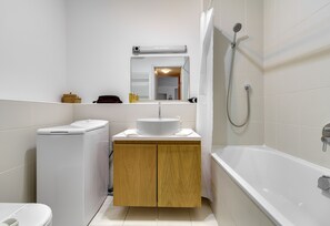 A modern bathroom with a toilet, washing machine, sink, and bathtub. - Quality Point Apartments 0-24 reception (Budapest)