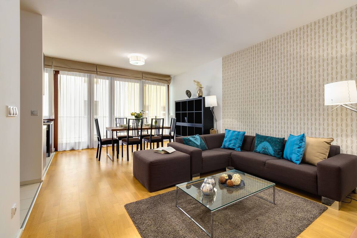 Una sala de estar moderna con un sofá seccional, una mesa de centro de vidrio y un comedor con una mesa y sillas.
