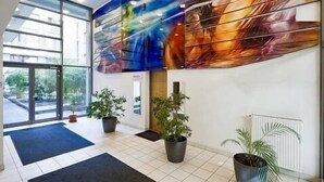 Un vestíbulo amplio con un cuadro abstracto de gran tamaño, plantas en macetas y vistas al exterior.