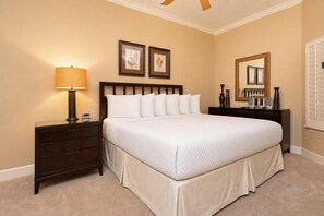 A neatly made bed in a hotel room with a bedside table, a lamp, framed artwork on the wall, and a mirror.