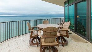 A round table with six chairs on a balcony with a view of the sea.