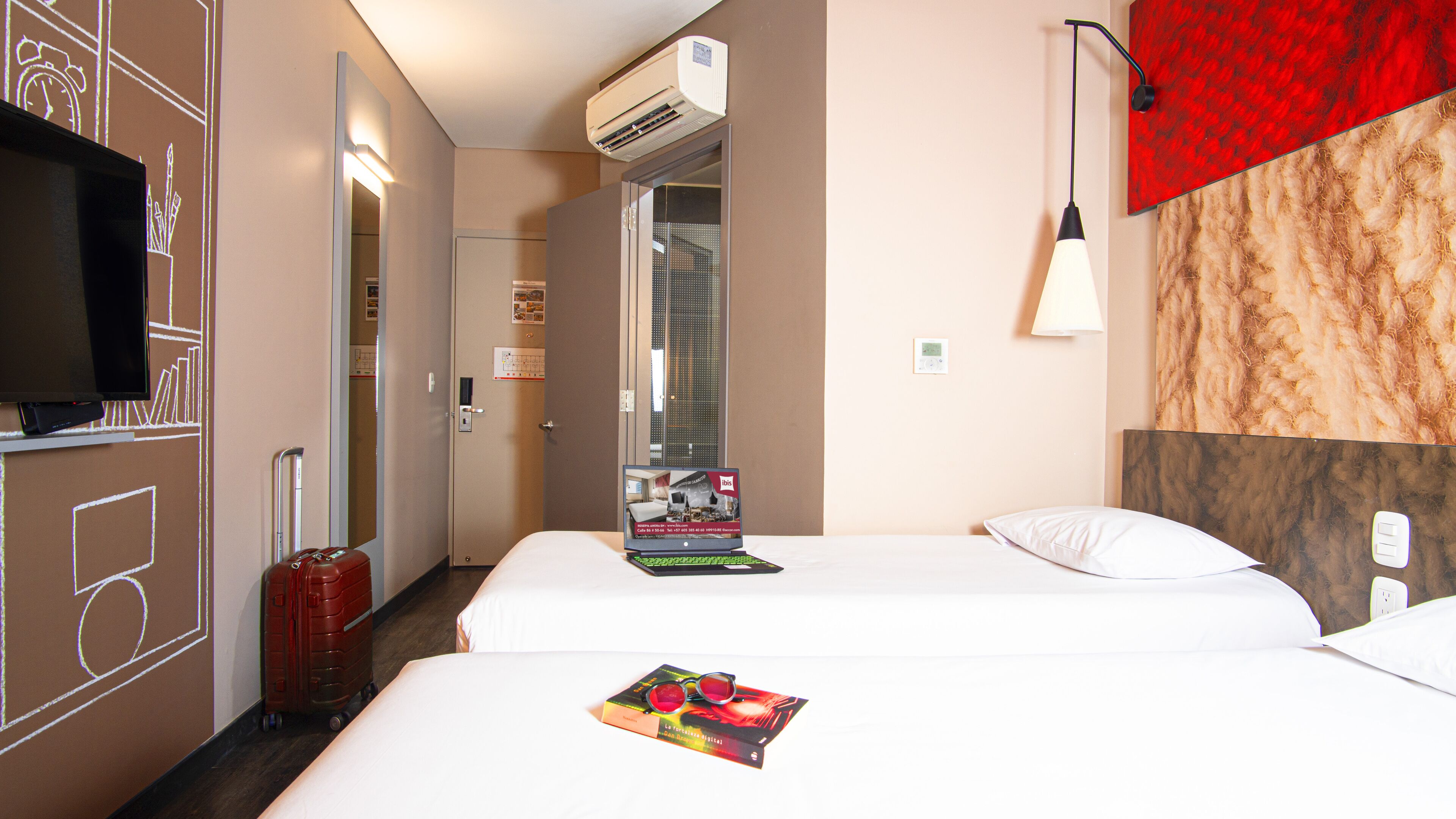 A hotel room with two beds, a TV, a red wall, and a door leading to a bathroom.