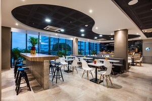 Zona de bar moderna con techo curvo, ventanas amplias y una combinación de taburetes y mesas.