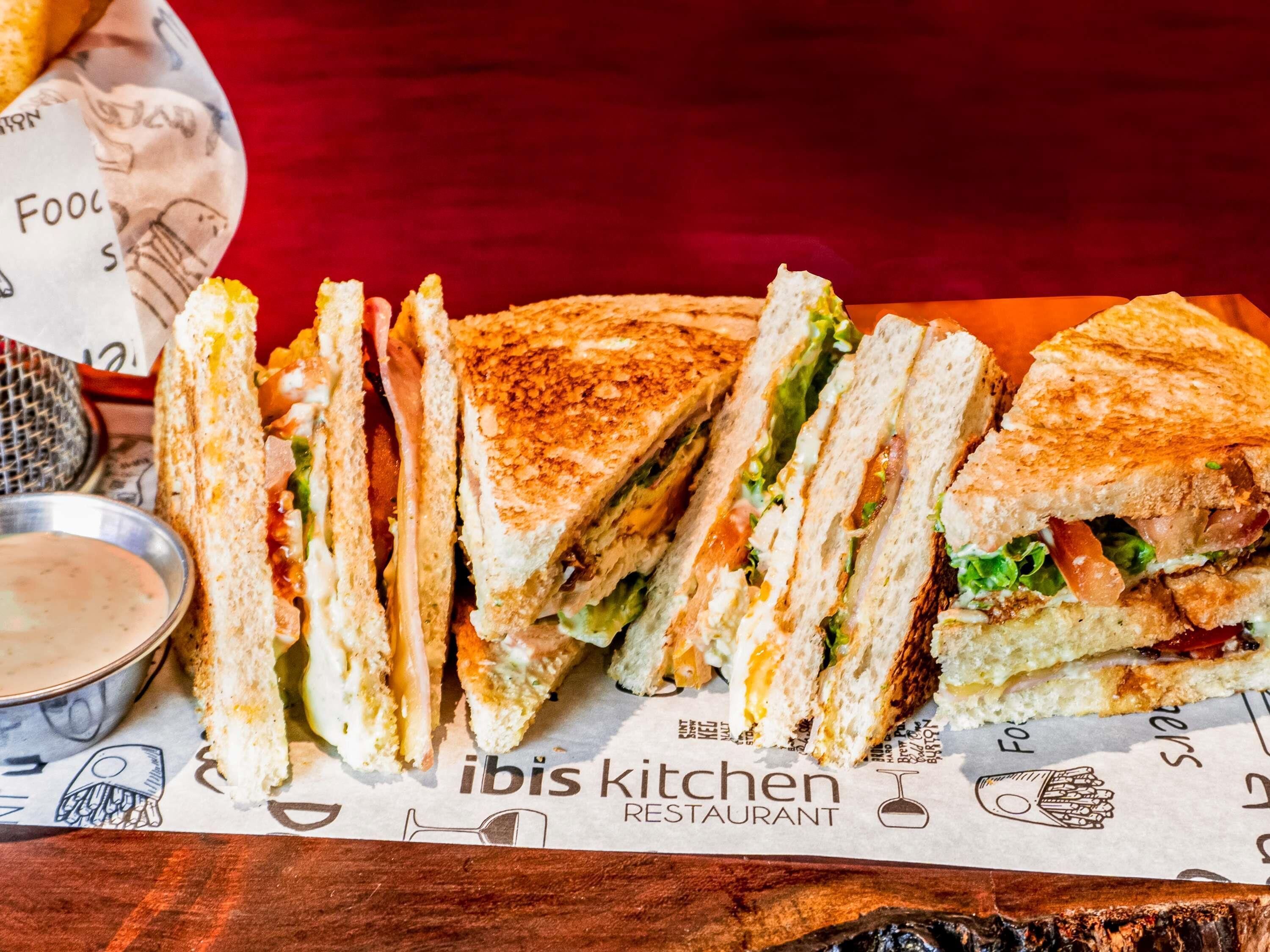 A sandwich with lettuce and tomato on a piece of paper with the text "ibis kitchen restaurant".