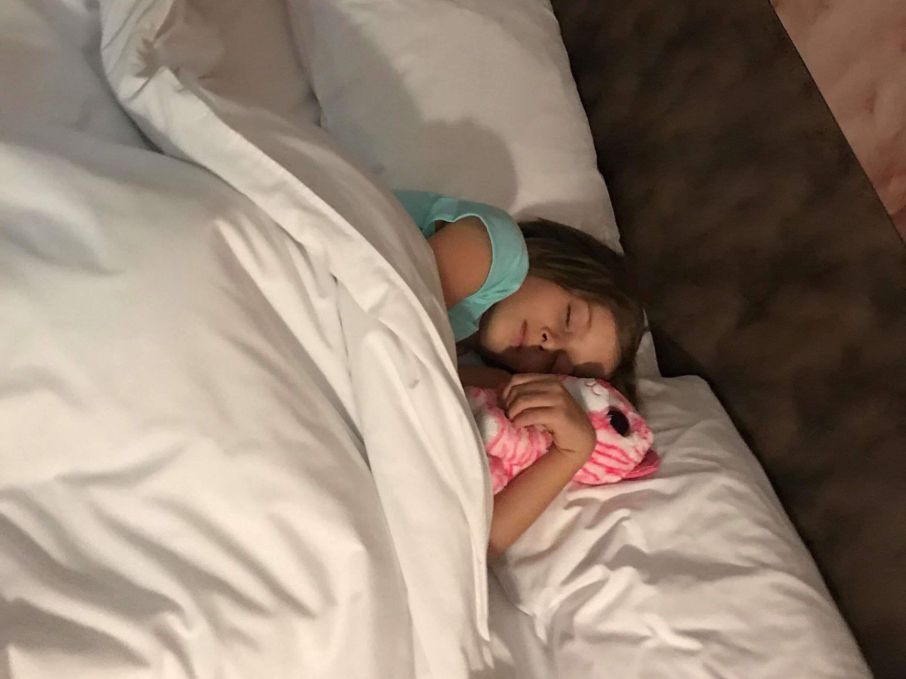 A person lying in bed with a white blanket and a pink stuffed toy.