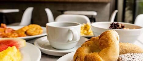 Une table à manger avec divers éléments pour le petit-déjeuner, notamment des viennoiseries, une tasse de café et une assiette de fruits.