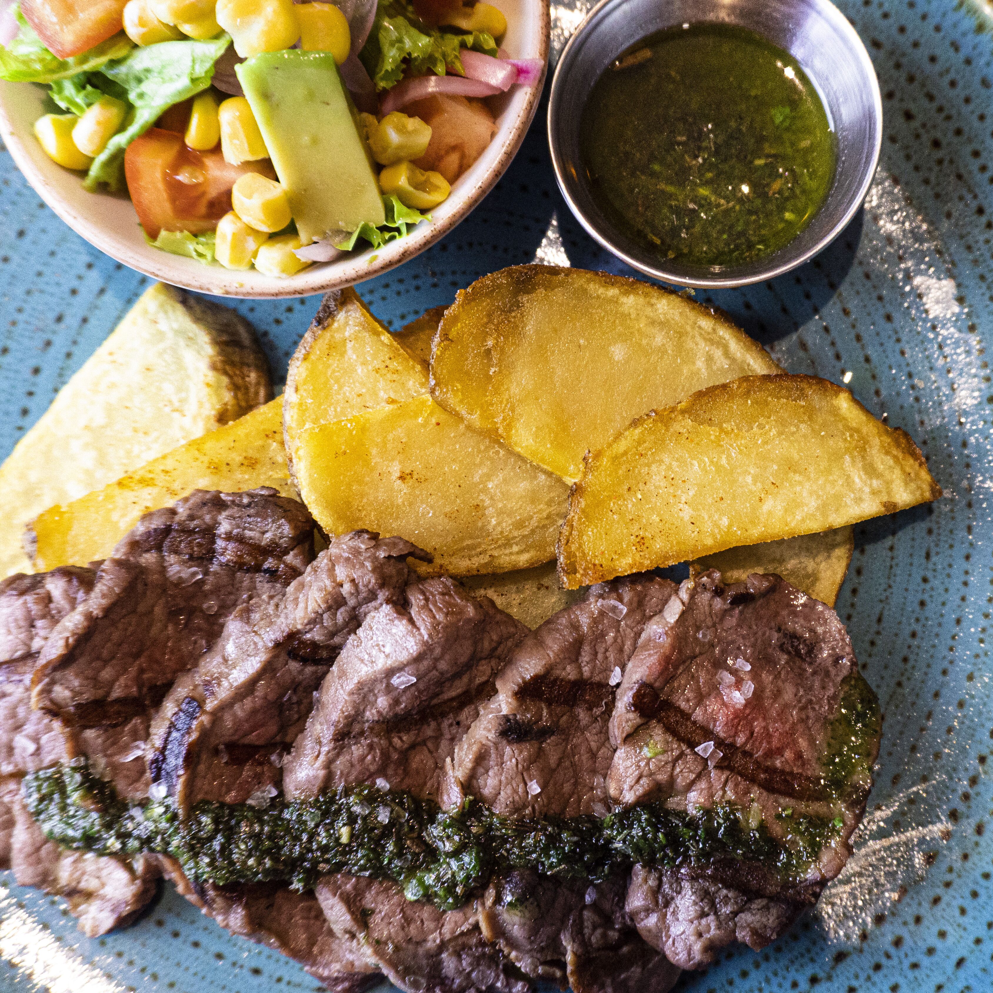 Un plato con filete, papas a la francesa, ensalada y una cazuela de salsa.