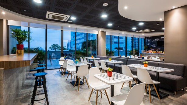 A modern restaurant with a bar area, white and black chairs, and tables with potted plants.