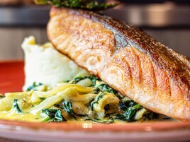 Un plato con un trozo de pescado, puré de patatas y un guiso cremoso de espinacas.