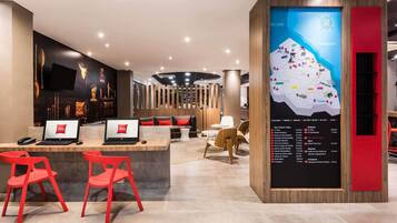 Een moderne hotellobby met een receptiebalie, rode stoelen en een groot scherm met een digitale kaart.