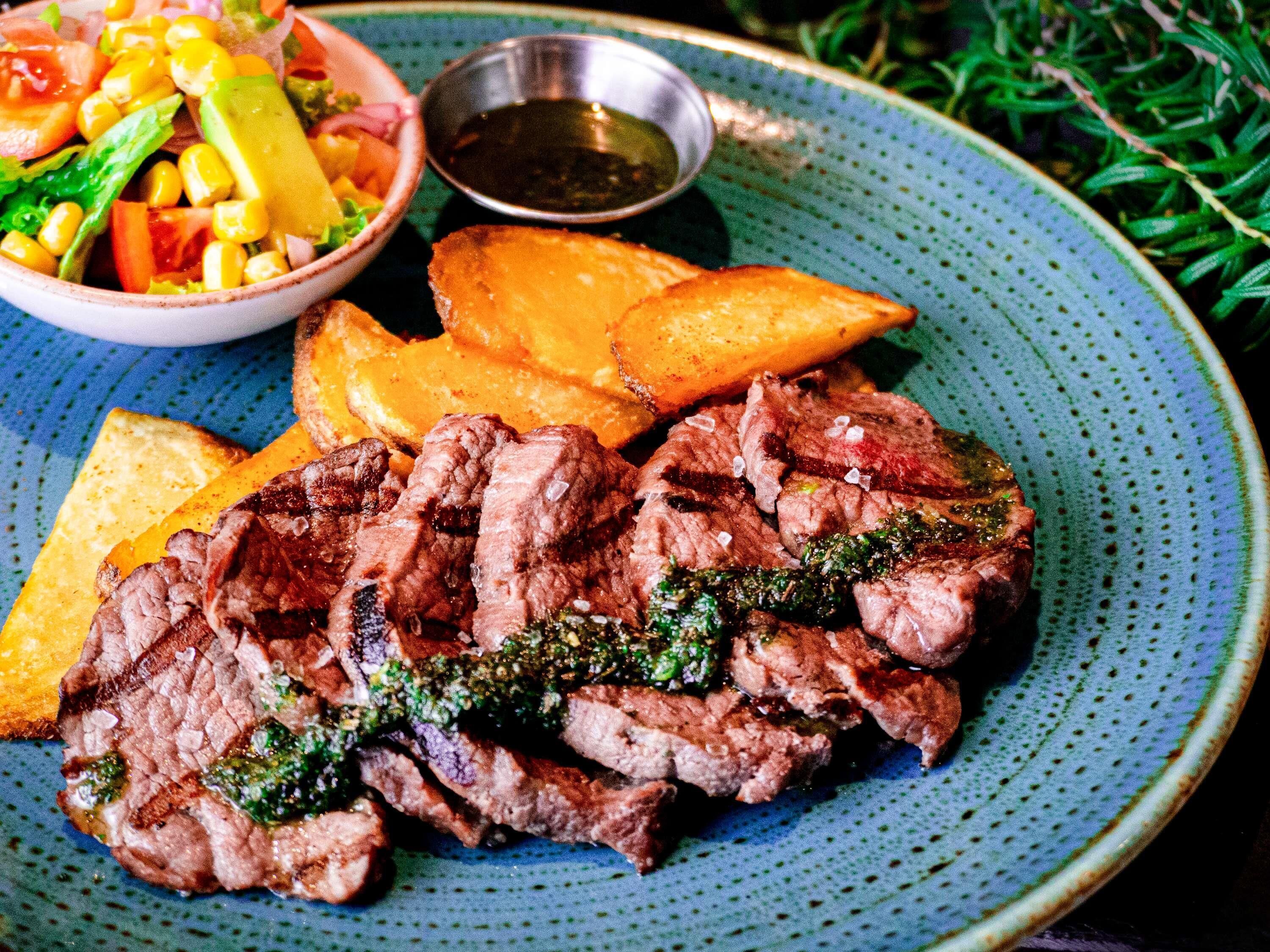 A plate of grilled steak with a side of roasted potatoes and a salad.