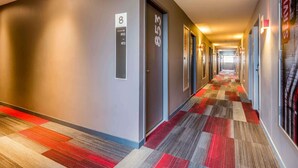 A hotel hallway with numbered doors, a patterned carpet, and a long corridor.