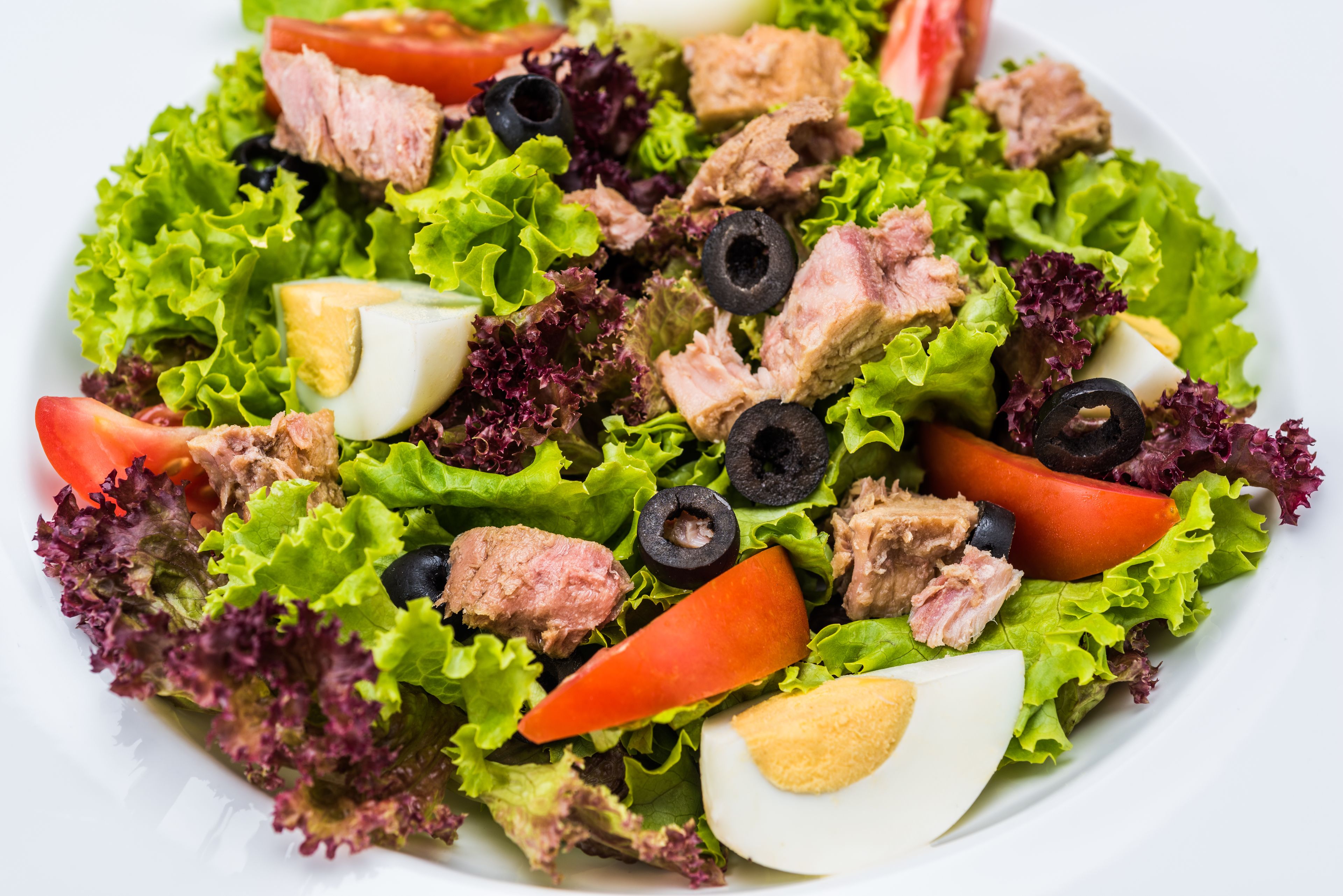 A salad with lettuce, tuna, olives, tomatoes, and hard-boiled eggs.