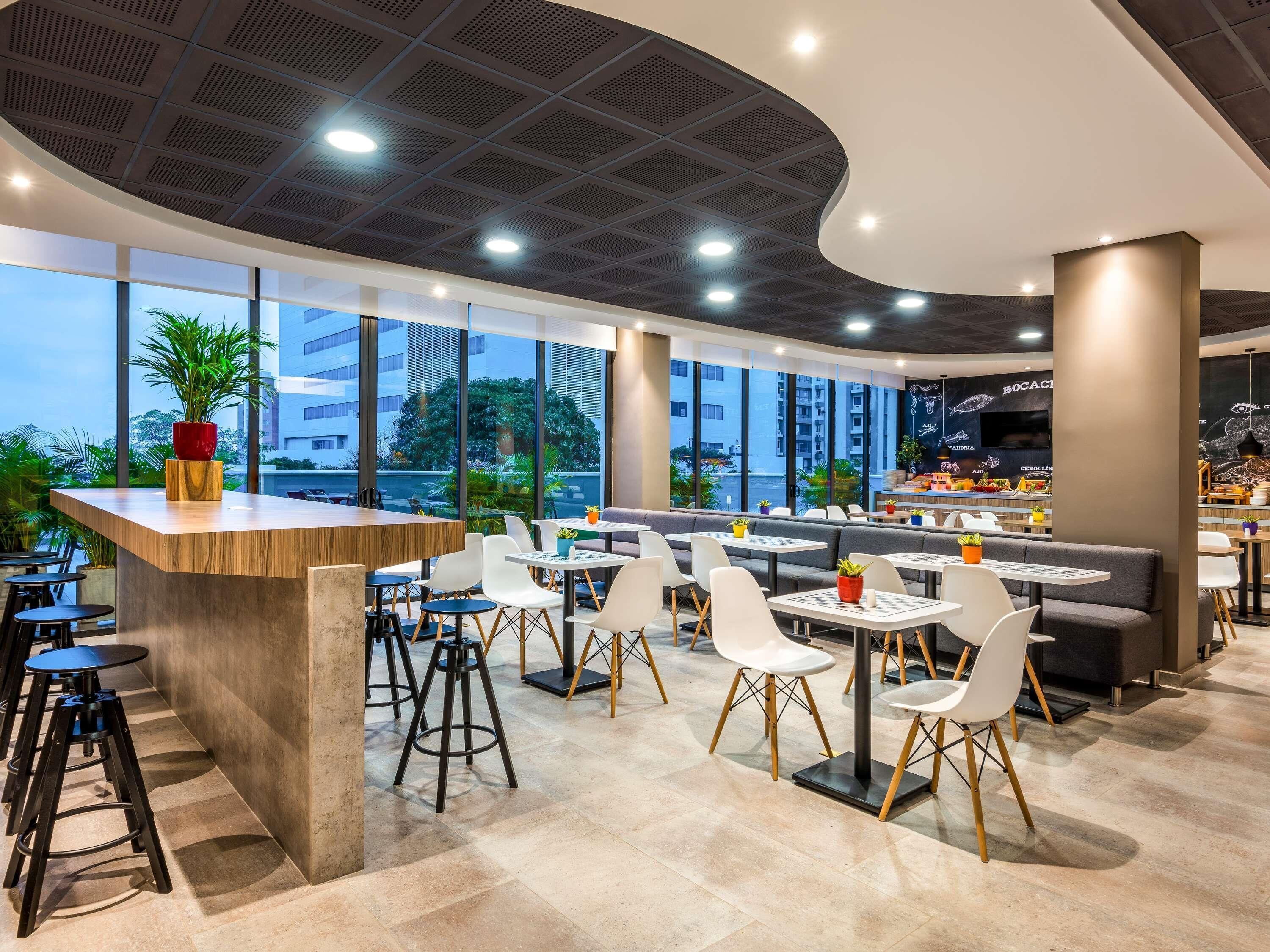 Un restaurante moderno con techo curvo, ventanas amplias y diversas opciones de asientos, incluyendo mesas y cabinas.