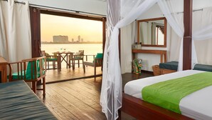 A room with a bed, a table, and chairs, a large window with a view of the city skyline, and a balcony with a table and chairs.