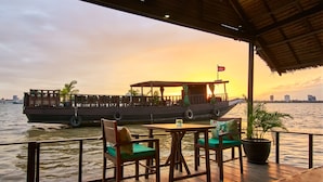A wooden deck with outdoor seating, a boat in the background, and a sunset view.