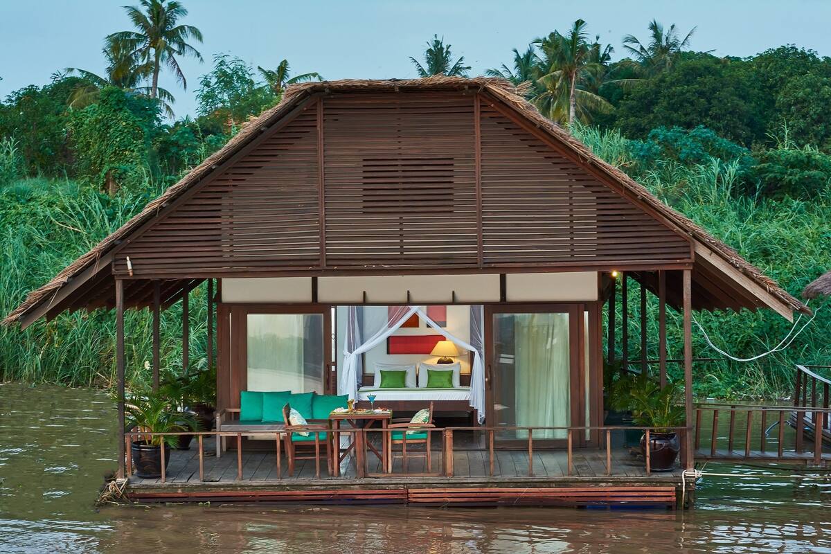 A wooden structure with a thatched roof, a bed with a canopy, and a small table with chairs.