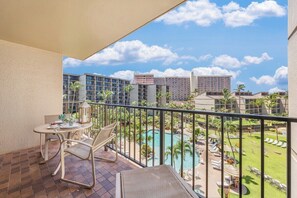A balcony with a table and chairs, overlooking a pool and resort area.