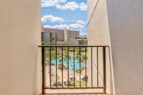 A view of a swimming pool with lounge chairs and palm trees, surrounded by buildings.