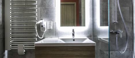 Un baño moderno con un lavamanos rectangular, cabina de ducha con mampara de vidrio y un perchero para toallas.