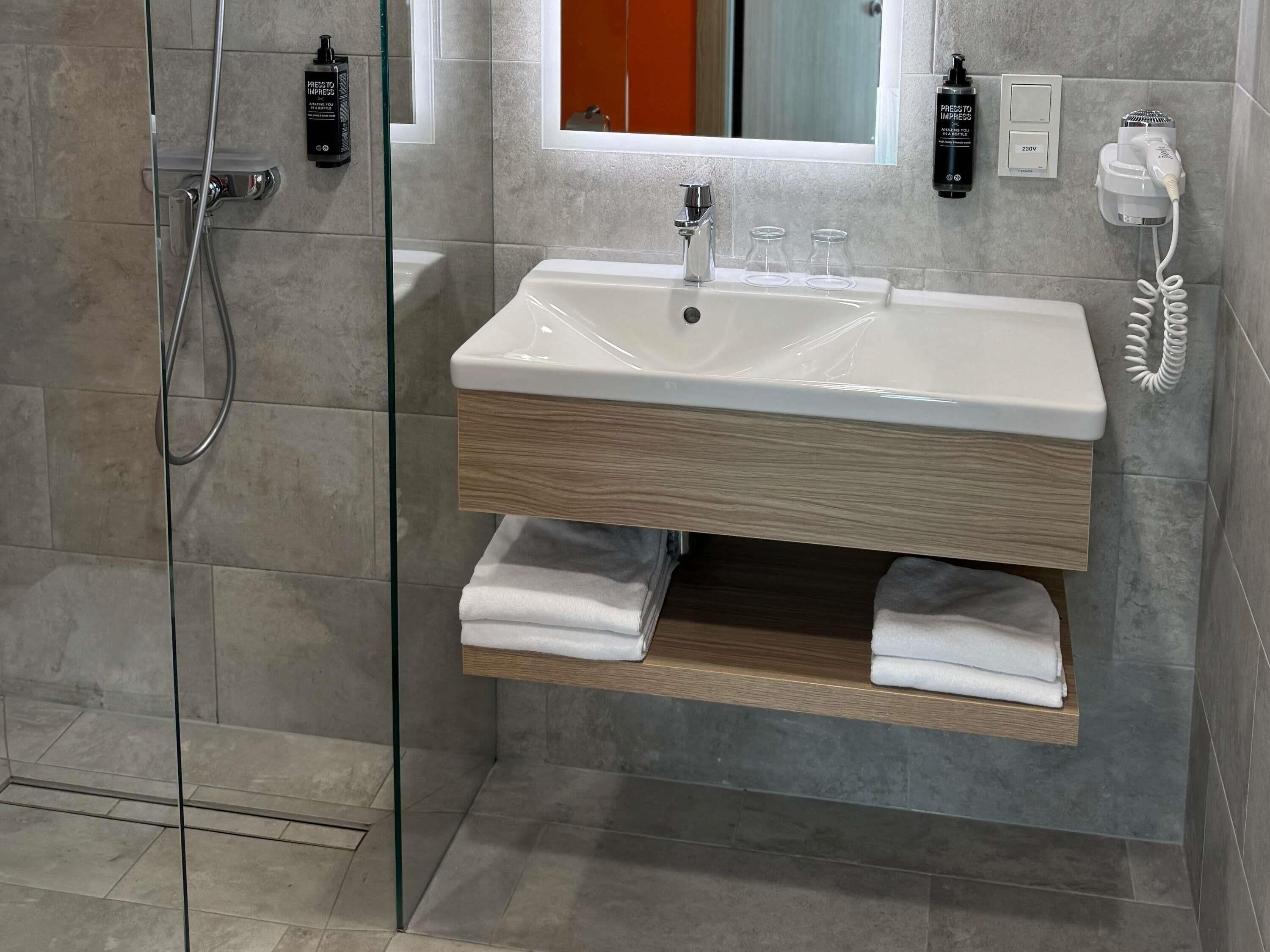 Ein modernes Badezimmer mit Duschkabine aus Glas, einem weißen Waschbecken mit Holzunterschrank und einem Handtuchhalter.