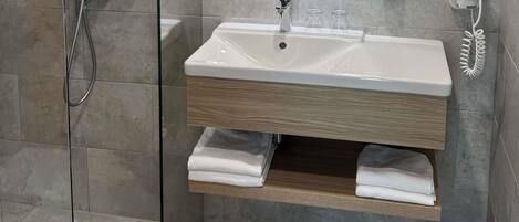 A modern bathroom with a glass shower enclosure, a white sink with a wooden vanity, and a towel rack.