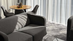 A modern hotel room with a grey sofa, a round dining table with chairs, and sheer curtains. - ibis Styles Warszawa City (Warsaw)