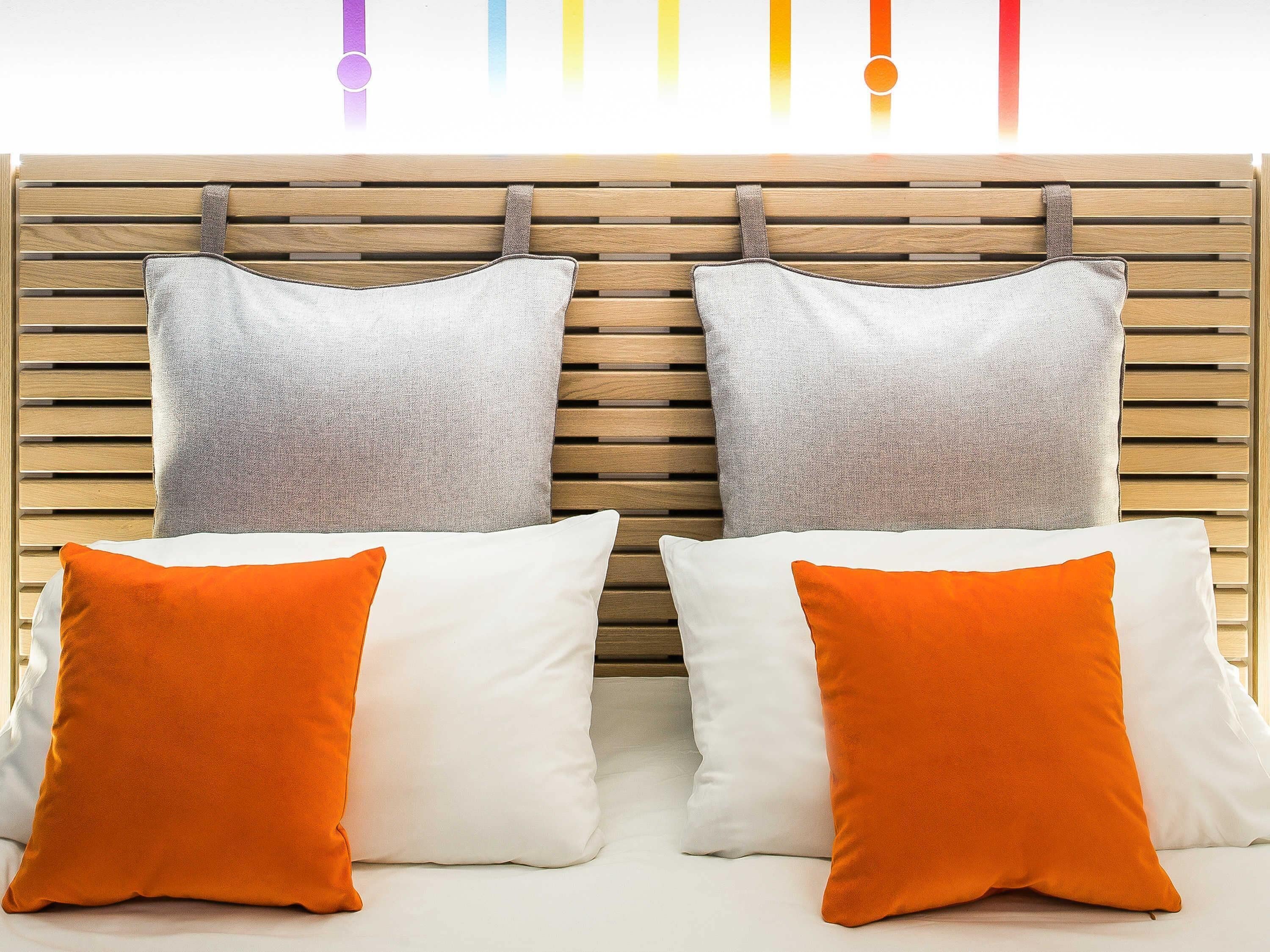 Een bed met twee kussens, één wit en één oranje, tegen een houten hoofdbord.
