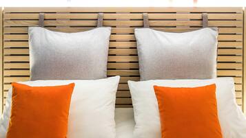 Una cama con dos almohadas, una blanca y otra naranja, frente a un cabecero de madera.