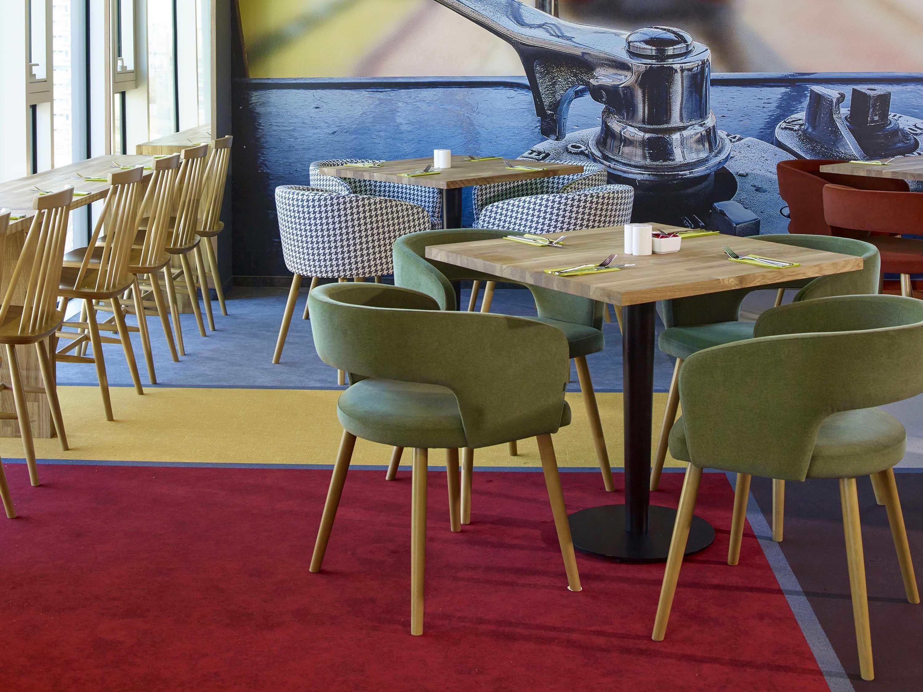 A restaurant interior with wooden tables and chairs, a red carpet, and a mural on the wall.