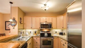 A modern kitchen with wooden cabinets, stainless steel appliances, and a granite countertop. - 1107 Trappeur's Lodge, Trappeur's Crossing Apartment 1 (Steamboat Springs)