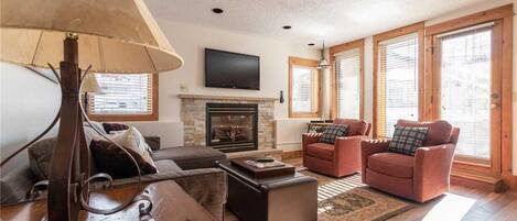 A living room with a fireplace, leather sofas, a coffee table, and a TV mounted on the wall.