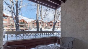 A covered outdoor area with metal chairs and a table, overlooking a snowy landscape with buildings in the background. - 1112 Trappeur's Lodge, Trappeur's Crossing Apartment 4 (Steamboat Springs)