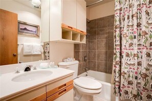 A bathroom with a white sink, toilet, and bathtub. There is a shower curtain with a forest pattern. - 1201 Trappeur's Lodge, Trappeur's Crossing Apartment 2 (Steamboat Springs)