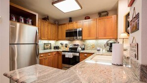 A kitchen with wooden cabinets, stainless steel appliances, granite countertops, and a built-in microwave. - 1201 Trappeur's Lodge, Trappeur's Crossing Apartment 2 (Steamboat Springs)