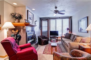 Un salon avec un canapé, des fauteuils, un téléviseur et un ventilateur de plafond.