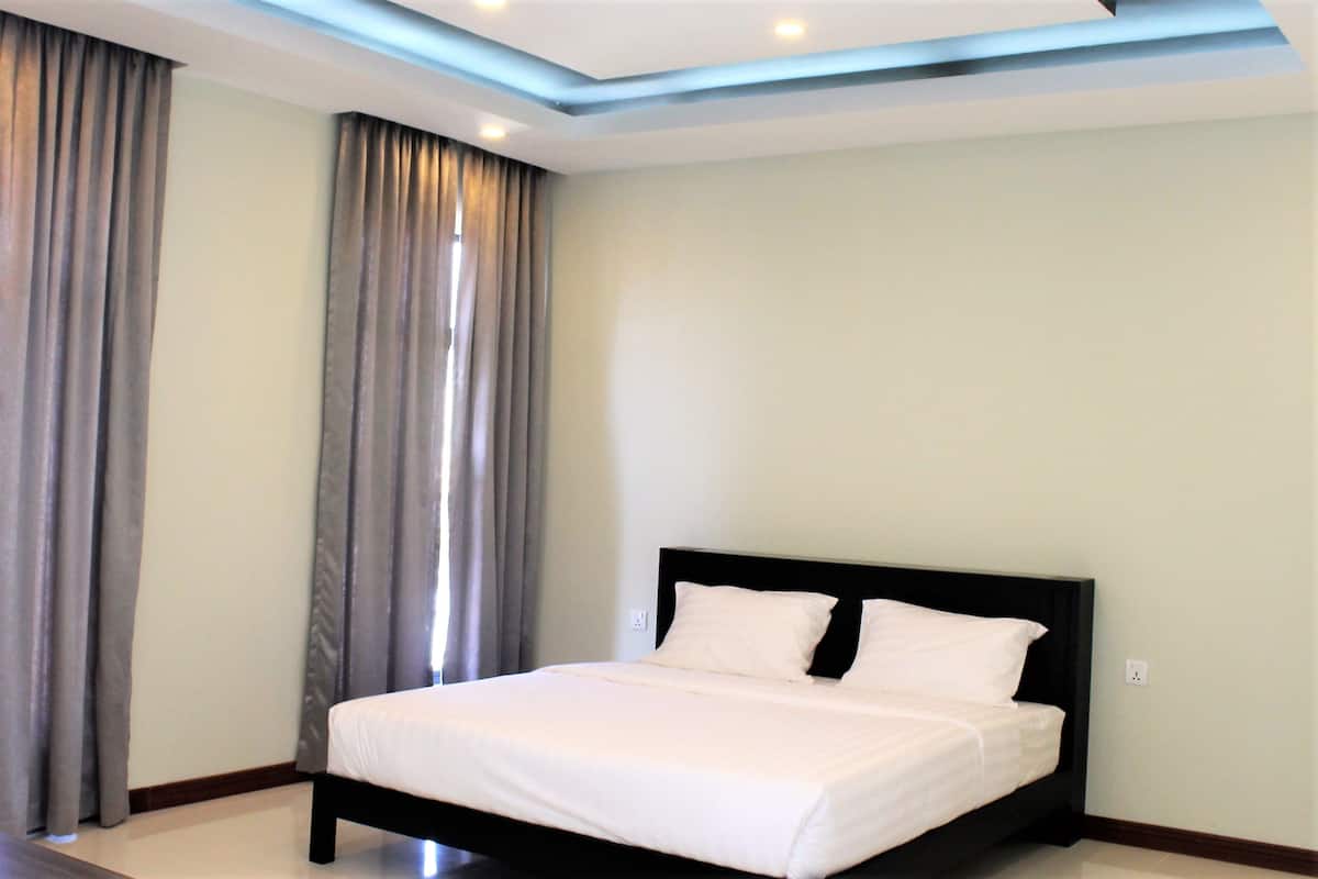 Een moderne hotelkamer met een groot bed, grijze gordijnen en inbouwspots.