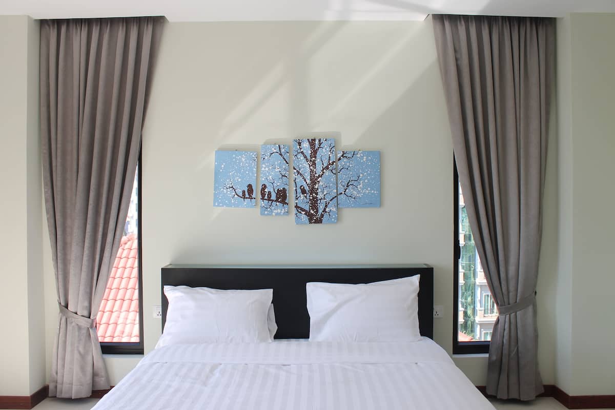 Hotelkamer met een bed, gordijnen en een kunstwerk aan de muur waarop een boom met vogels staat afgebeeld.
