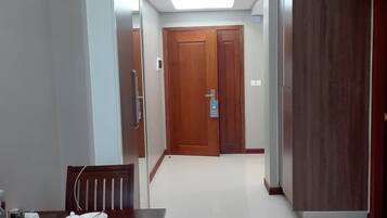 A dining area with a table set for two, a wooden door in the background, and a hallway leading to another room.