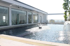 Une piscine sur le toit, avec une eau cristalline, entourée de murs en verre et d’un bâtiment moderne.