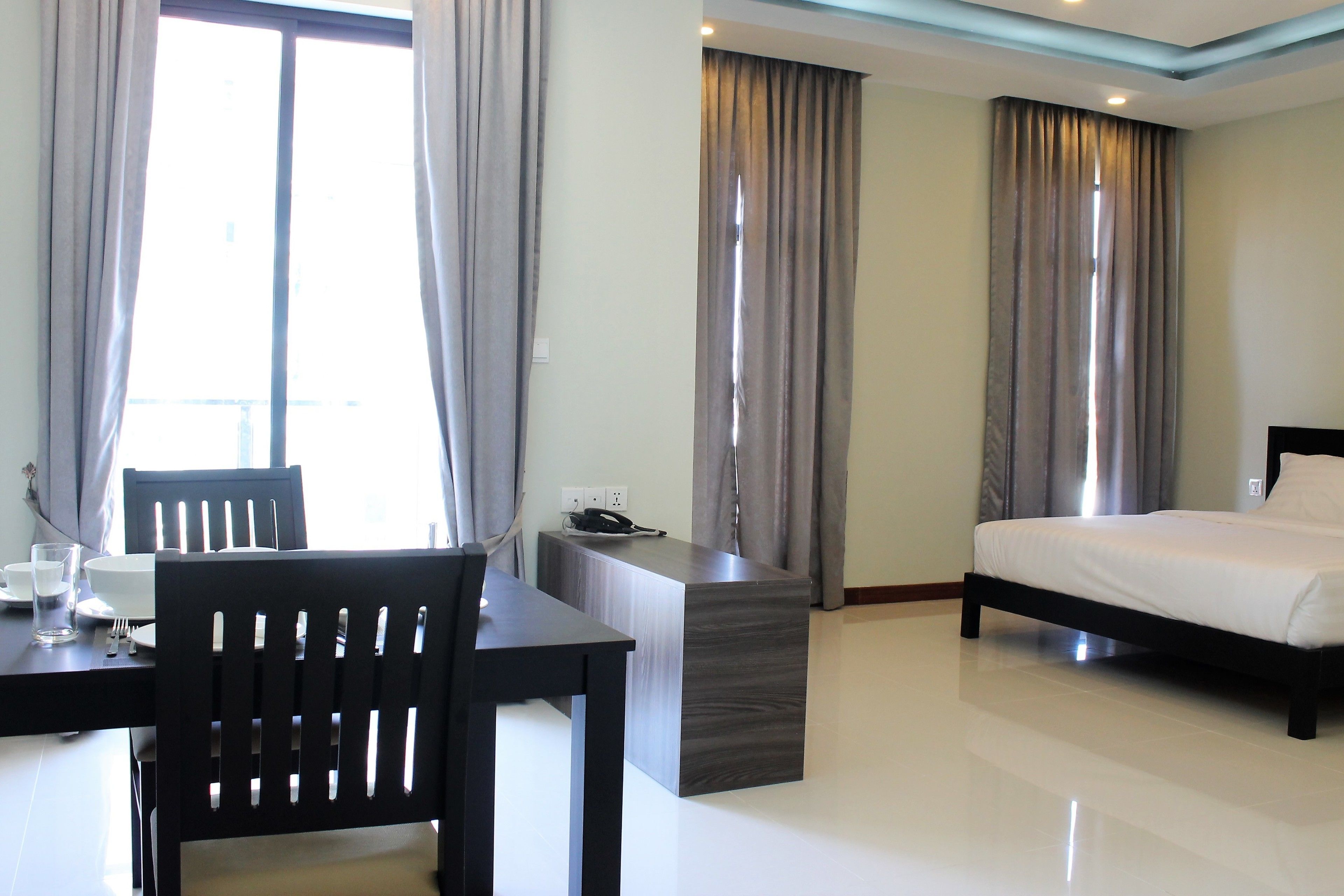 Habitación de hotel con cama, escritorio con silla, mesita con teléfono y cortinas en las ventanas.