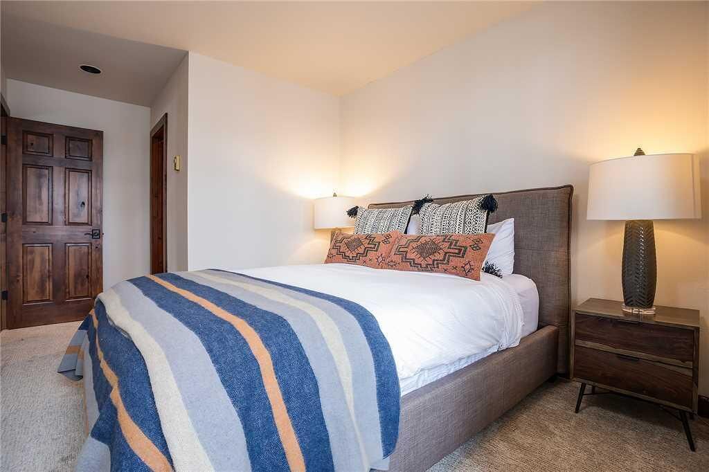 A bedroom with a bed, two bedside lamps, a wooden door, and a nightstand.