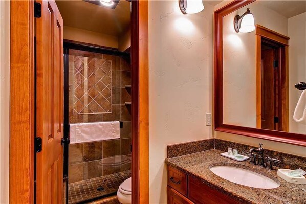 A bathroom with a wooden vanity, a sink, a mirror, and a shower area.