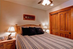 A bedroom with a wooden bed, two bedside lamps, a ceiling fan, and a wooden wardrobe.