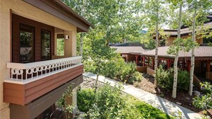 A building with a balcony, surrounded by trees and a garden. - 1210 Trappeur's Lodge, Trappeur's Crossing Apartment 1 (Steamboat Springs)