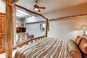 Ein Schlafzimmer im rustikalen Stil mit einem Holz-Kopfteil, Deckenventilator und einem Bett mit gestreifter Bettwäsche.
