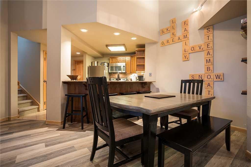 Une cuisine moderne avec des meubles en bois, un four à micro-ondes et une cuisinière. On y trouve une table à manger avec des chaises, ainsi qu’un mur décoré de lettres de Scrabble formant des mots.