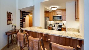 A kitchen with wooden cabinets, a granite countertop, and a central island with bar stools. - 1303 Trappeur's Lodge, Trappeur's Crossing Apartment 2 (Steamboat Springs)